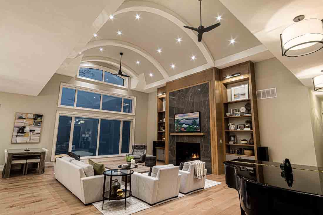 Modern living room with vaulted ceiling, large windows, white seating, and a stone fireplace