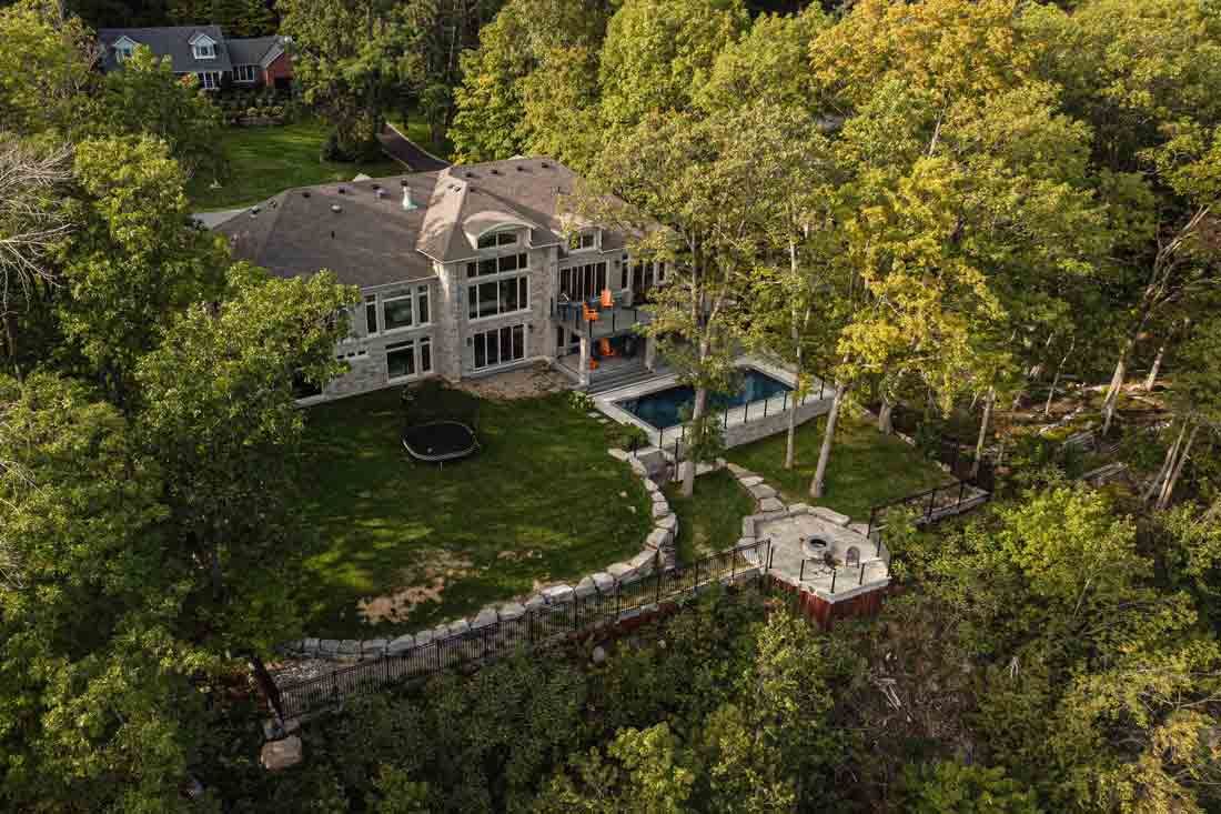 Aerial view of a large stone house nestled in dense green trees beside a terraced garden and patio.