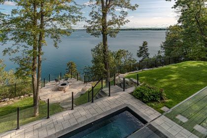 Lakefront patio with pool, stone steps, and green lawn overlooking calm water and trees