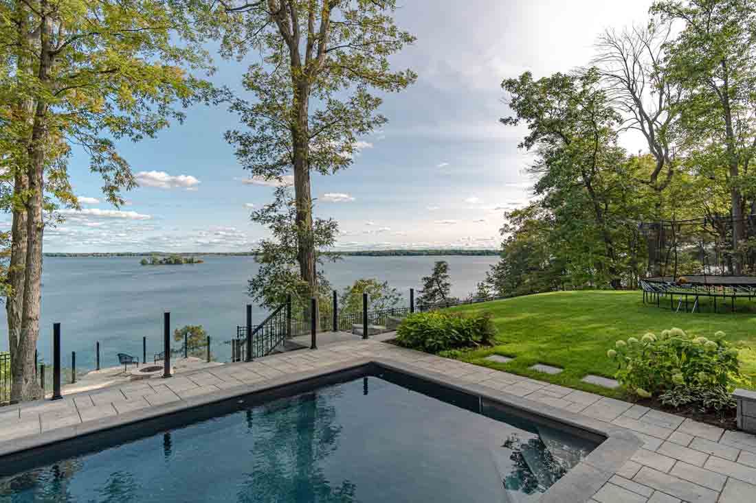 Backyard pool beside a lake, with lawn, trees, and clear water view