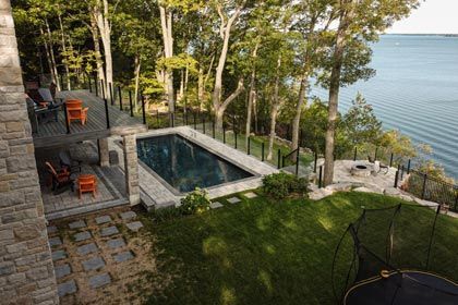 Modern lakeside patio with a small pool, stone steps, trees, and grassy lawn overlooking the water
