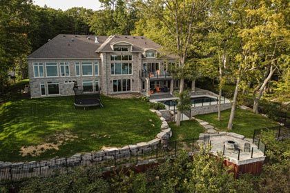 Large lakeside house with stone terrace, green lawn, and wooded shoreline