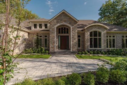 Stone-brick house with arched entryway, paved front path, and manicured landscaping