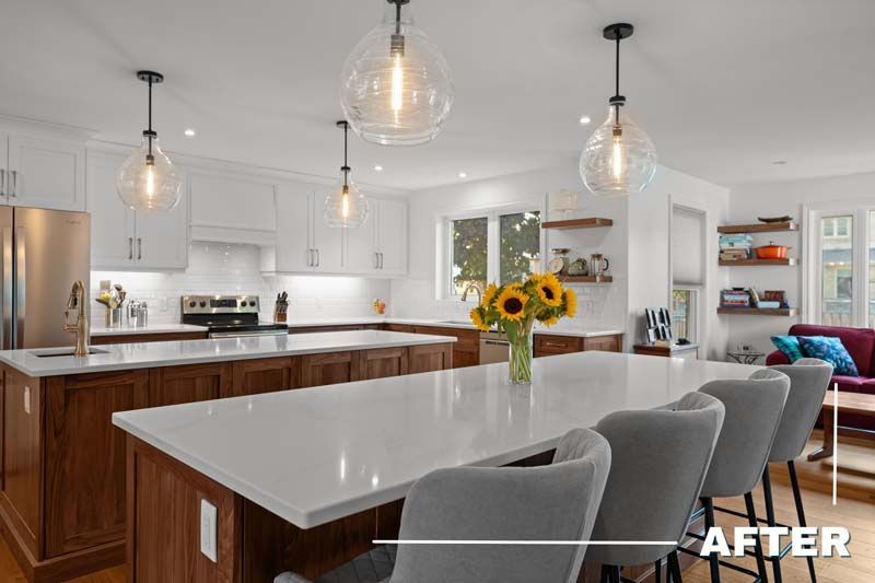 Bright white kitchen with wood island, pendant lights, gray stools, and a vase of sunflowers on the counter.