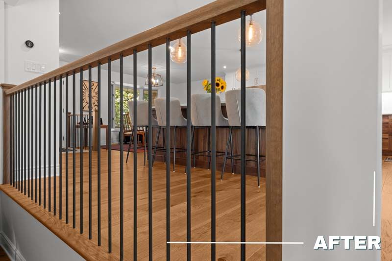 Staircase railing with dark metal balusters and wood handrail overlooking a bright dining area