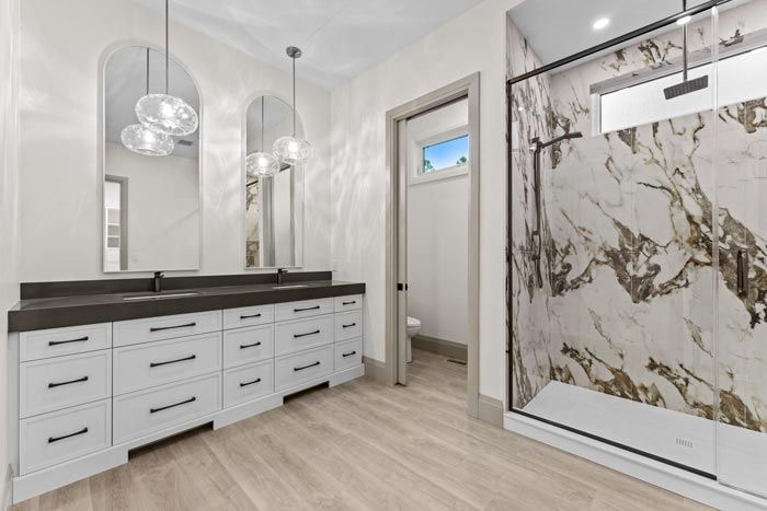 Modern bathroom with double vanity, large mirror, glass shower, and marble-pattern tile accent wall
