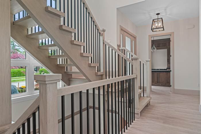 Modern foyer with staircase, black railing, light wood floors, and hallway opening to a bathroom