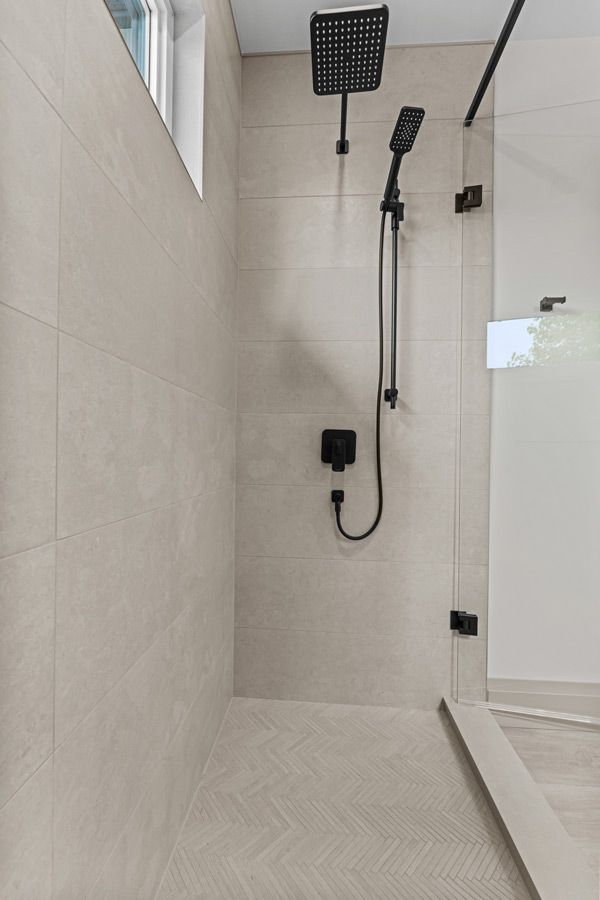 Modern tiled shower with glass door, rainfall showerhead, and handheld shower on a wall panel