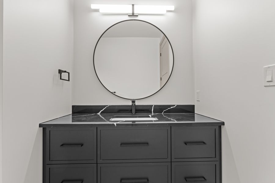 Modern bathroom vanity with round mirror, black countertop, and dark cabinets.