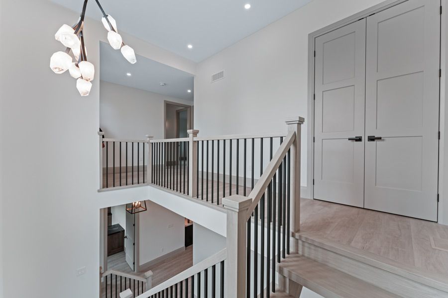 Bright foyer with white railings, chandelier, and closed double doors on an upper landing