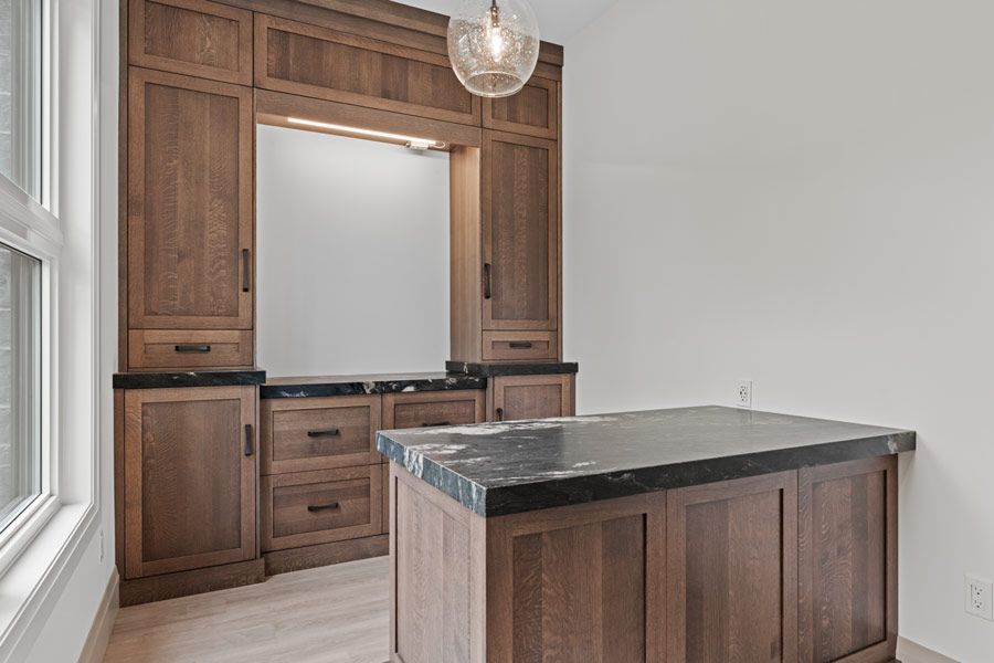 Wood-paneled kitchen nook with cabinets, a black-topped island, and a hanging light fixture