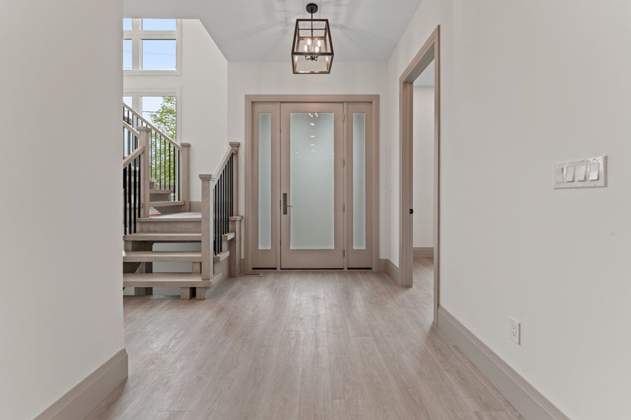 Bright empty foyer with light wood floors, staircase, double front doors, and a hanging lantern.