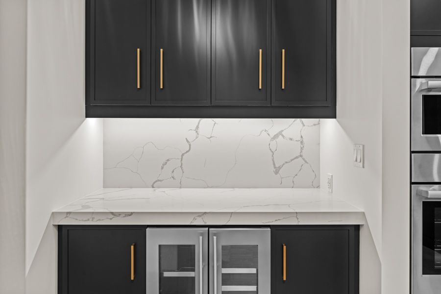 Modern kitchen nook with dark cabinets, white marble backsplash, and built-in wine fridge under a countertop.