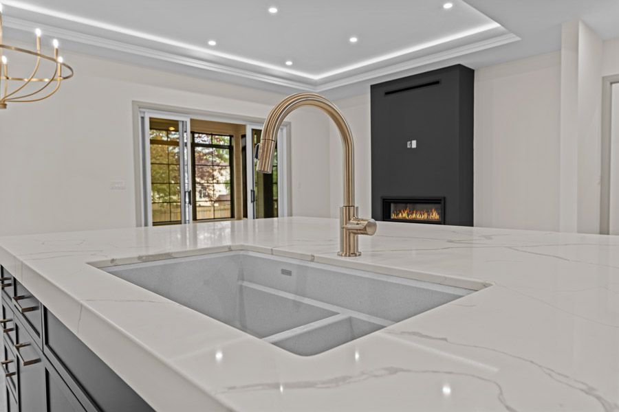Modern white kitchen with marble island, gold faucet, and a black fireplace wall