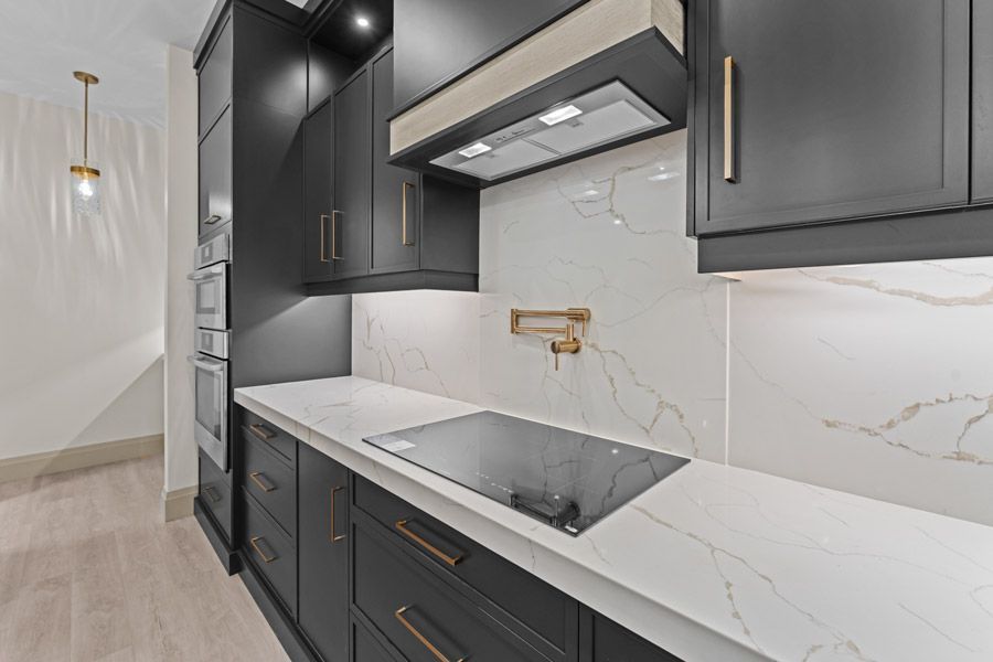 Modern kitchen with black cabinets, marble backsplash, white countertops, and built-in cooktop