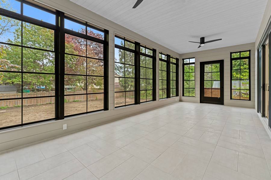 Bright sunroom with black-framed windows, white tile floor, and ceiling fans, overlooking a backyard.
