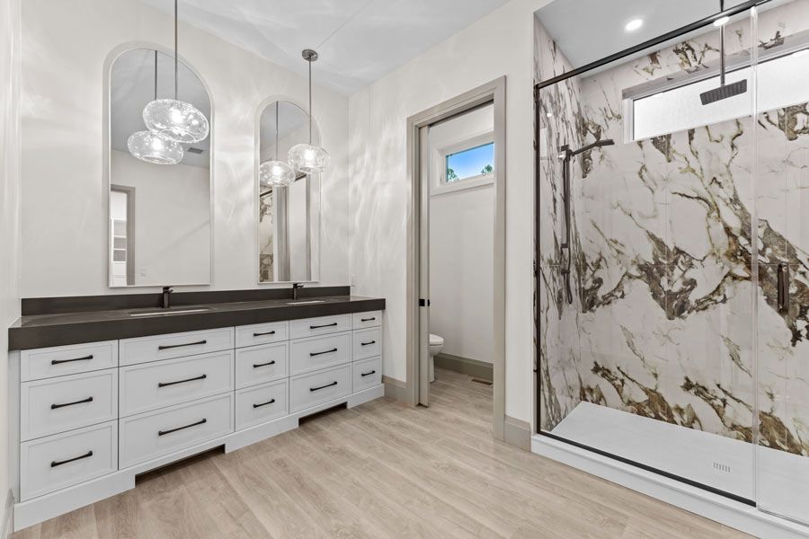 Modern bathroom with double vanity, large mirror, pendant lights, and marble-pattern shower door.