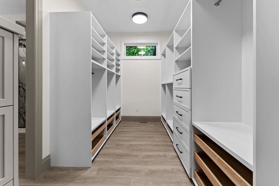 Bright walk-in closet with white shelving, drawers, and wood floor under a ceiling light.