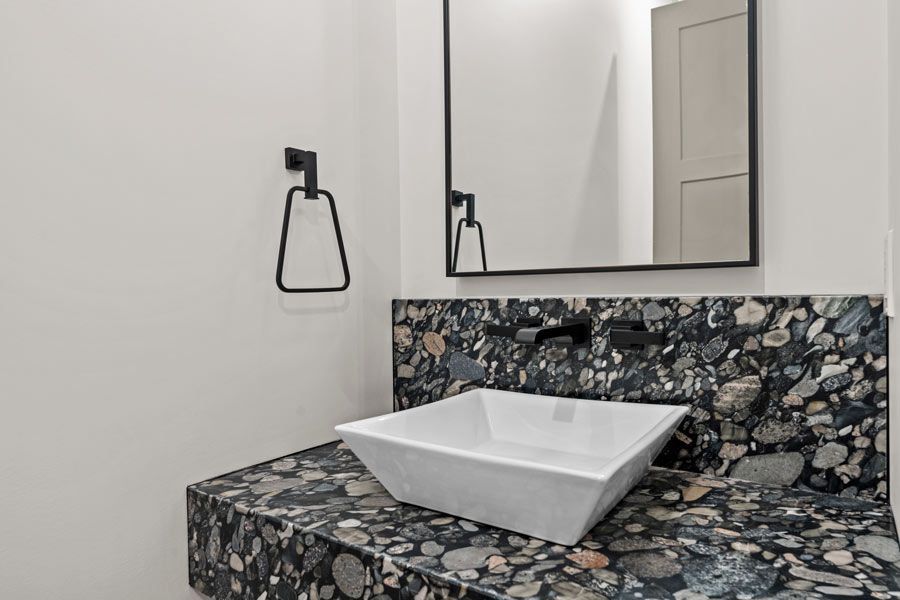 Modern bathroom vanity with square vessel sink, dark stone countertop, and wall mirror on white walls