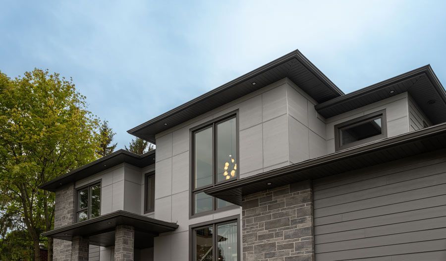 Modern two-story house exterior with gray siding, stone accents, and large windows under a cloudy sky