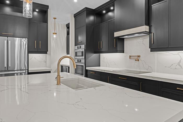 Modern kitchen with black cabinets, marble island, stainless appliances, and gold faucet