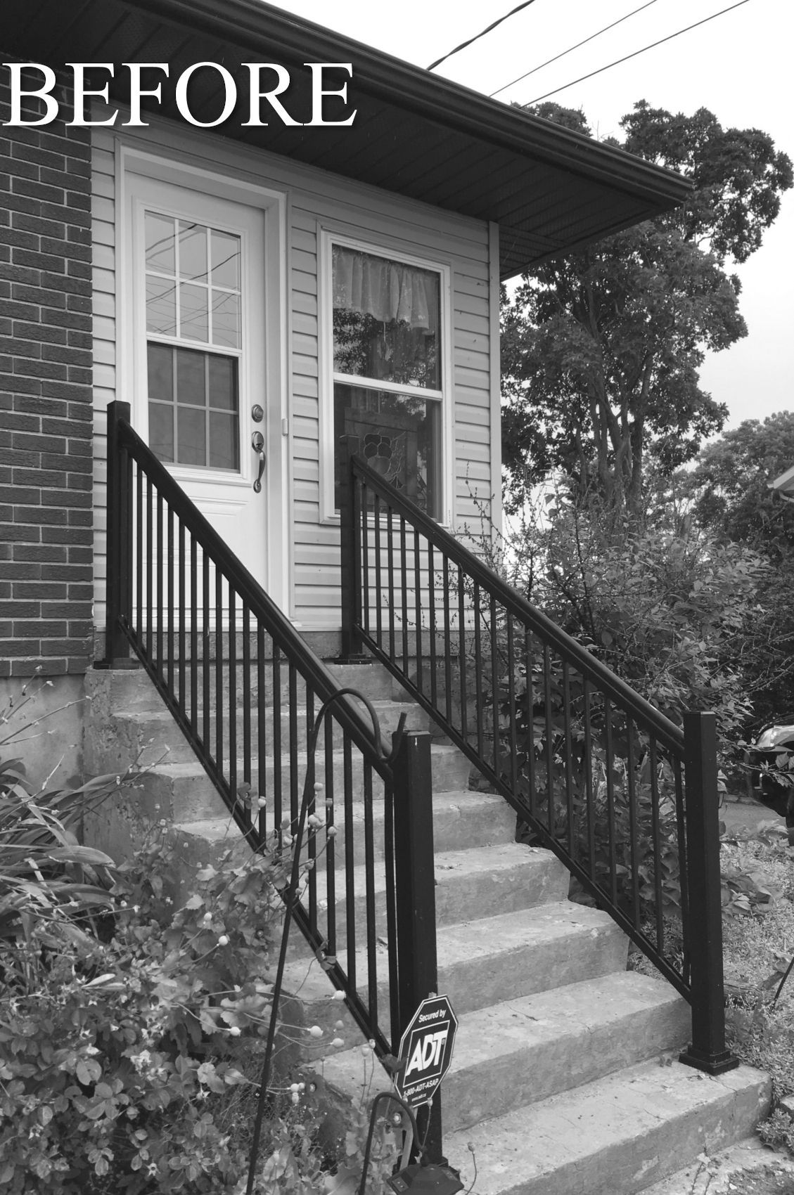 Before photo of a brick house entrance with concrete steps and black railings.