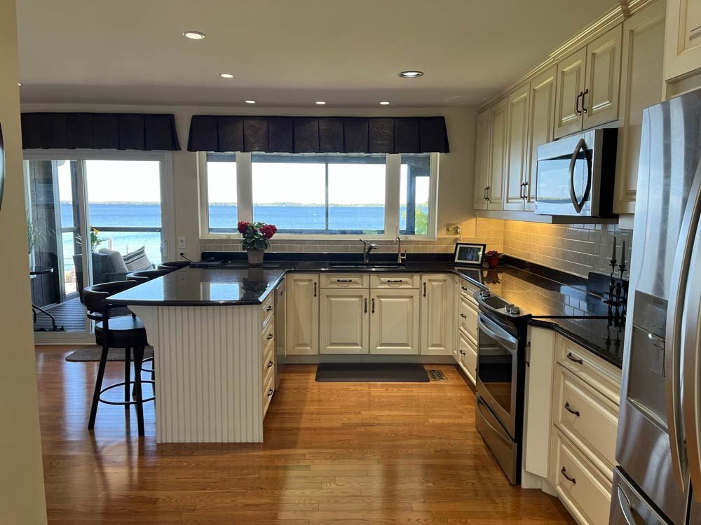 Bright modern kitchen with black counters, white cabinets, and large windows overlooking the water.