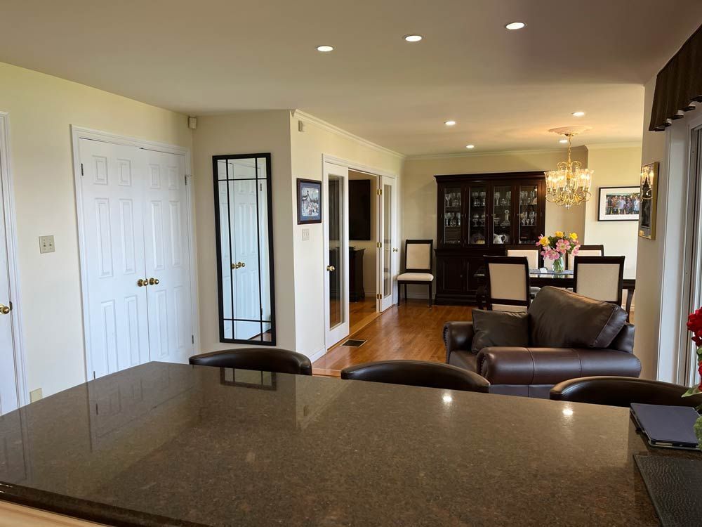 Modern kitchen opening to a living room with leather chairs, white doors, and recessed ceiling lights.