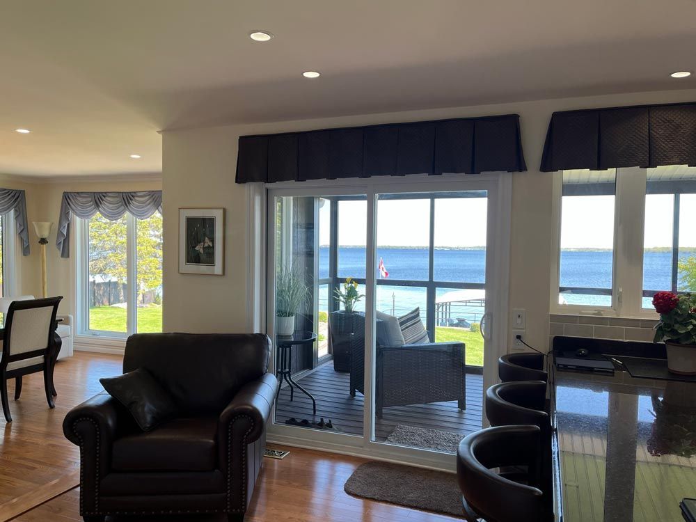 Bright living room with leather chairs, glass table, and sliding doors opening to a water view.