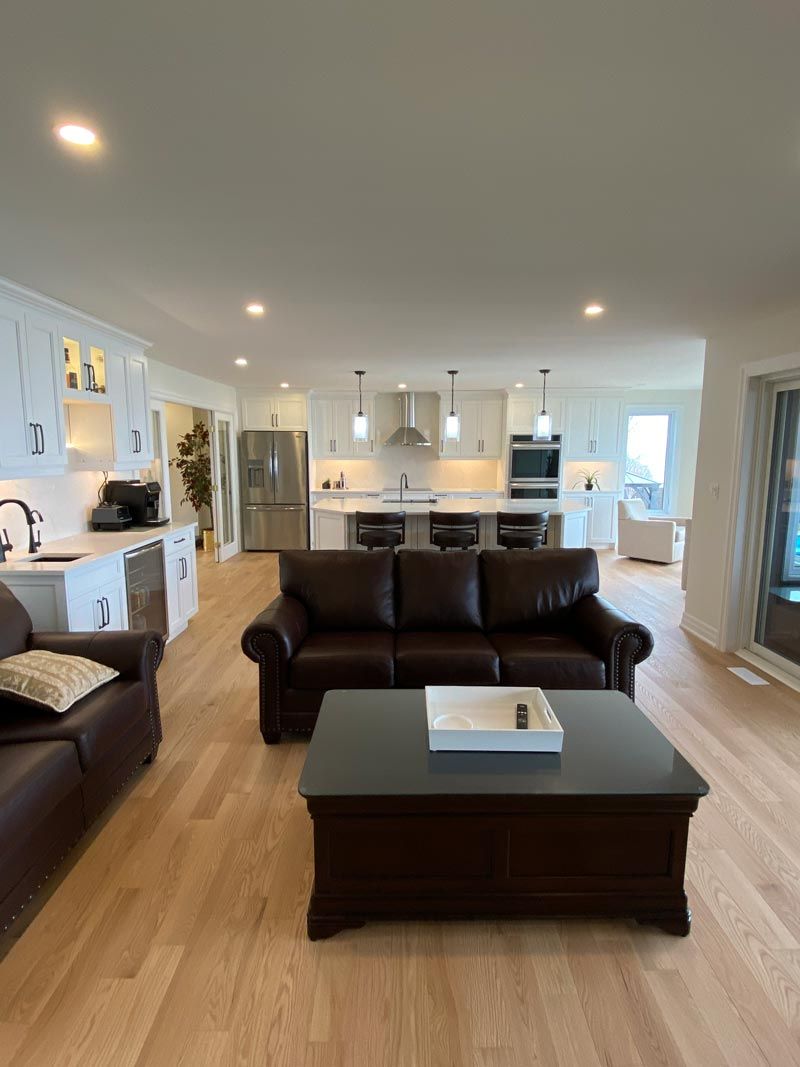 Bright open-plan living room with brown sofas, coffee table, and white kitchen in the background