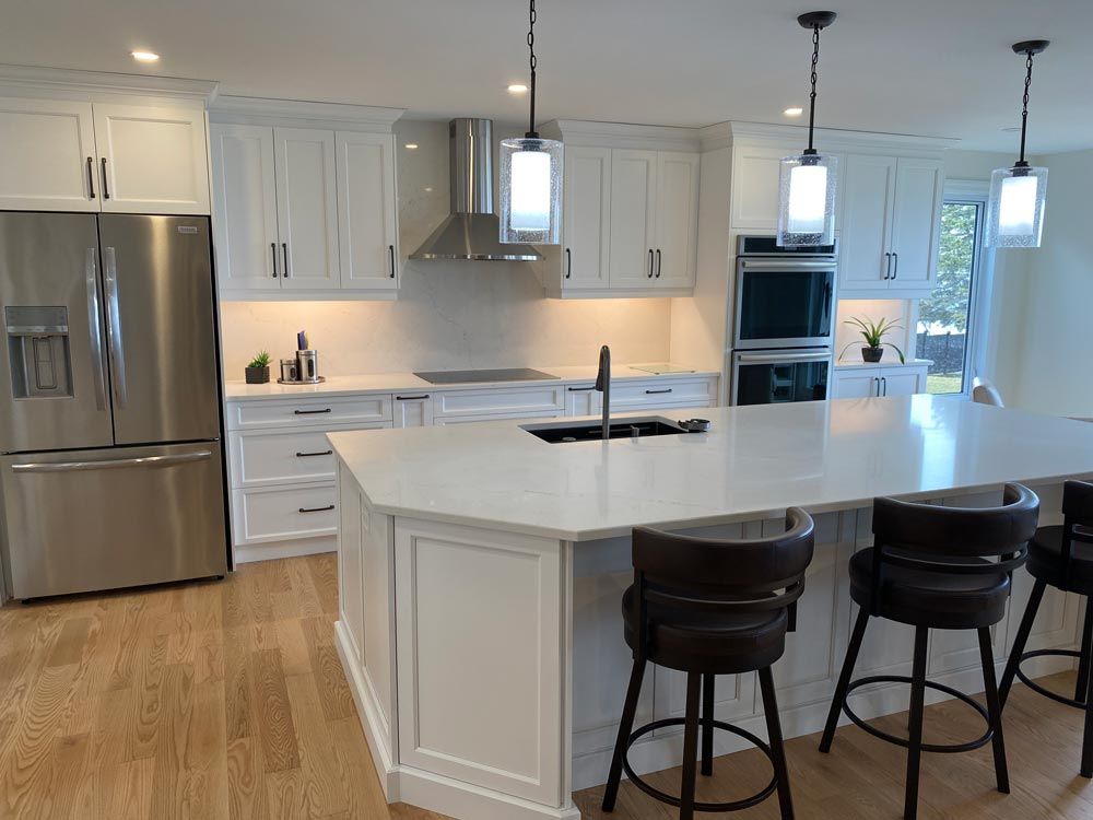 Modern white kitchen with island, bar stools, stainless steel fridge, and pendant lights