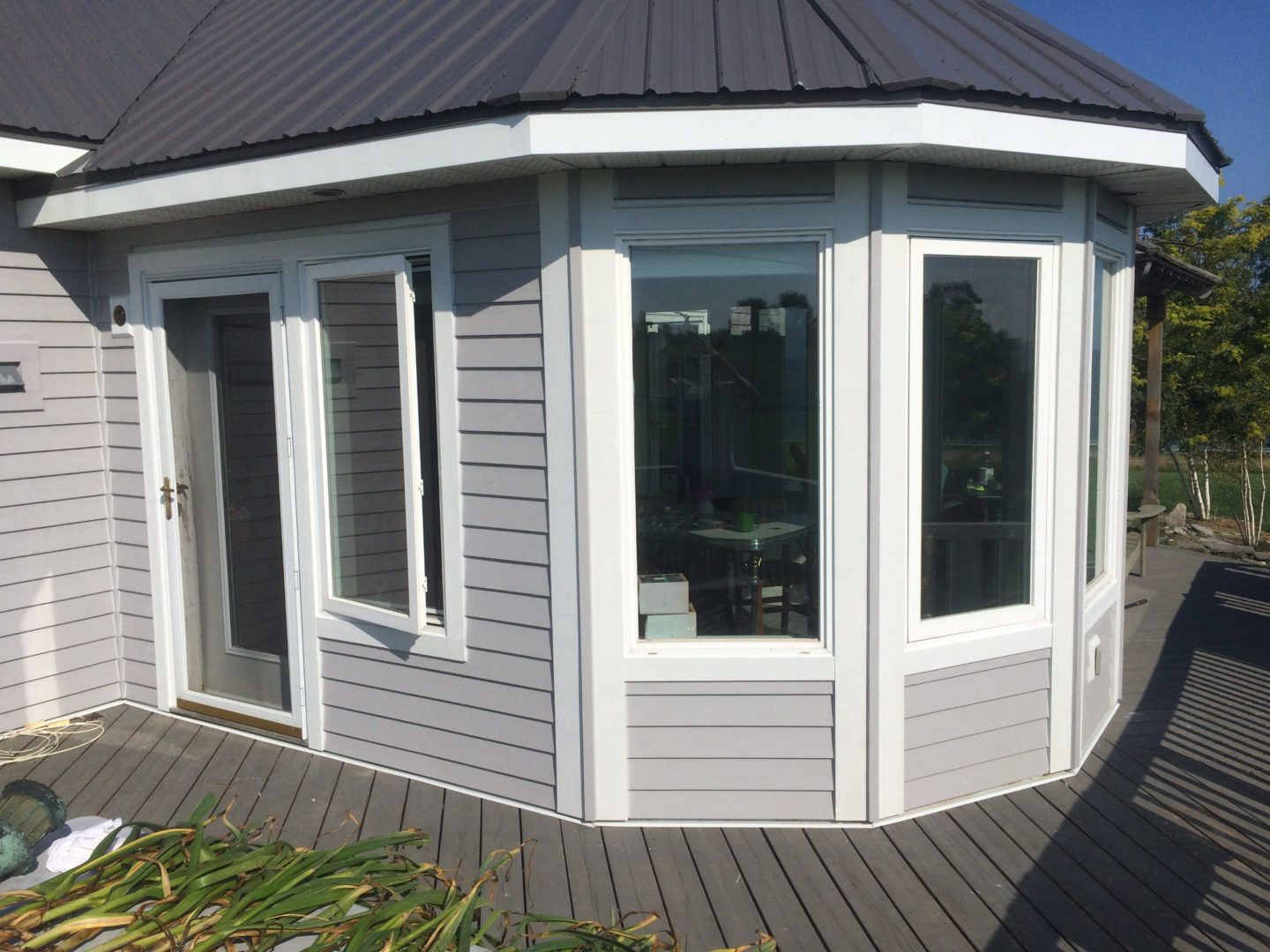 Round white sunroom with large windows and dark roof on a wooden deck
