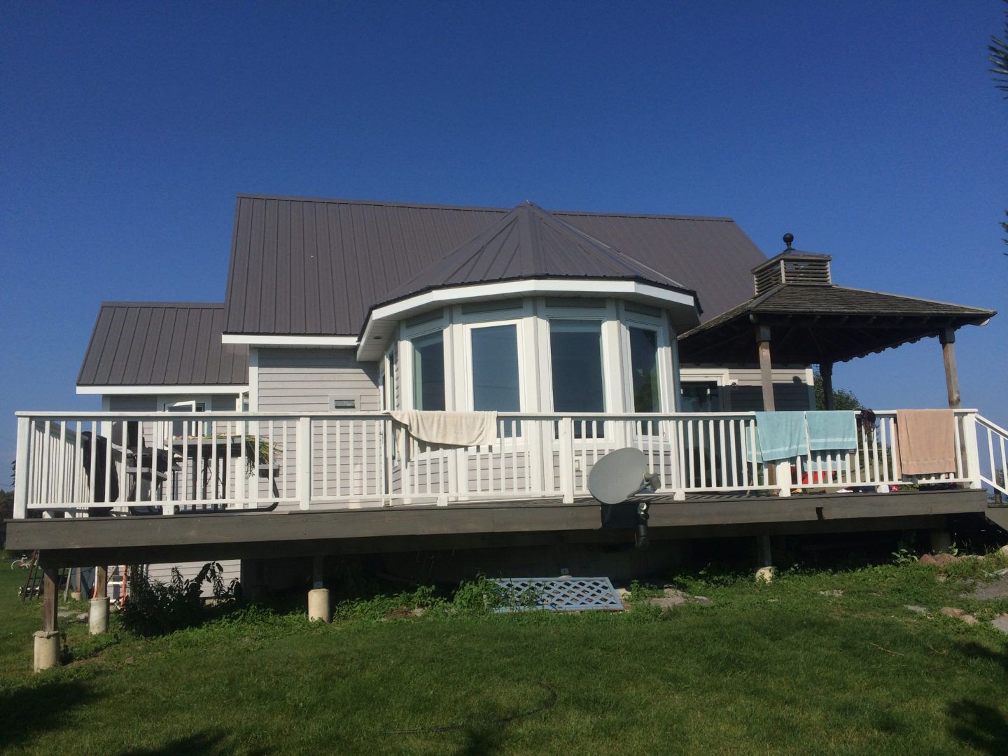 House with large white deck on a grassy hillside under a clear blue sky