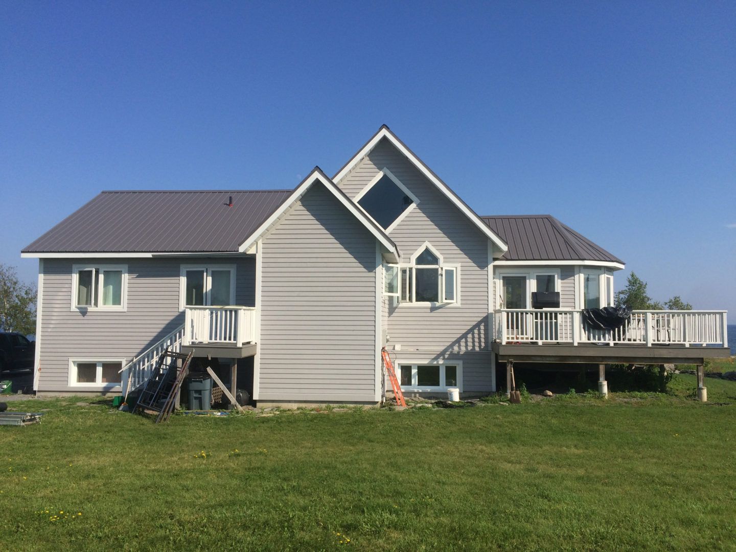 Gray house with two decks and a central gable on a grassy lawn under a blue sky