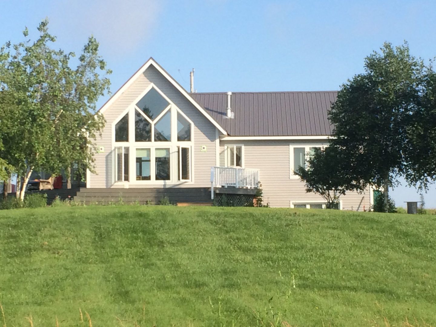 House with large windows on a grassy hill under a clear blue sky