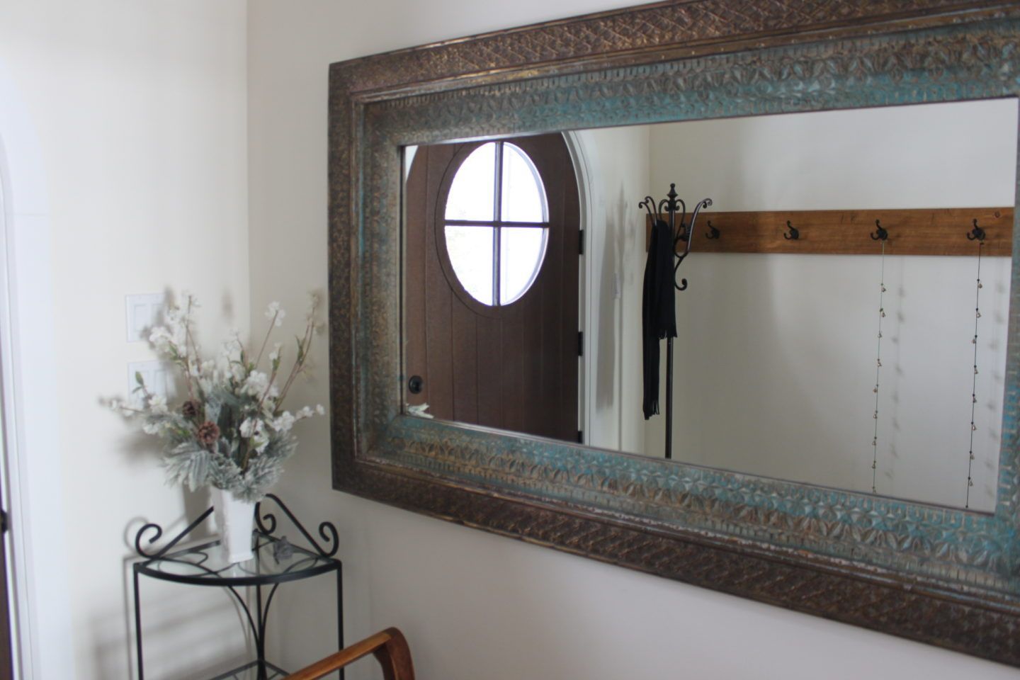 Wall mirror above a small table with flowers in a bright entryway