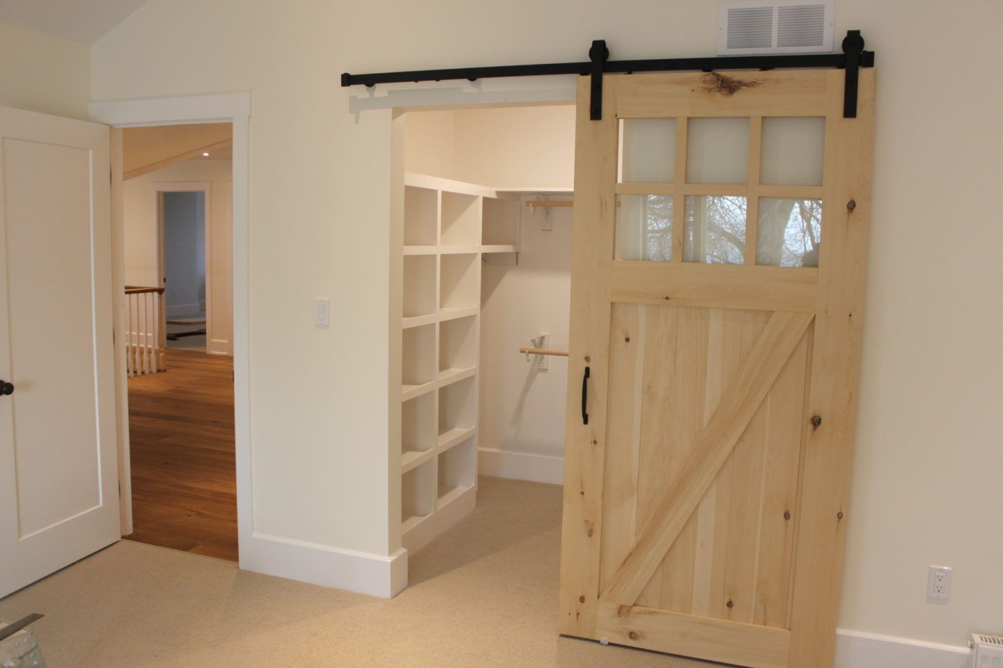 Barn interior with a sliding wooden door open to a small white closet and hallway.
