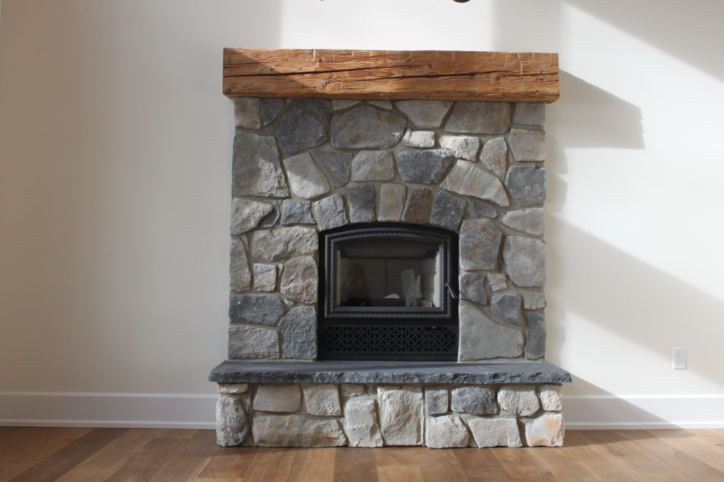 Stone fireplace with wooden mantel and black insert against a white wall
