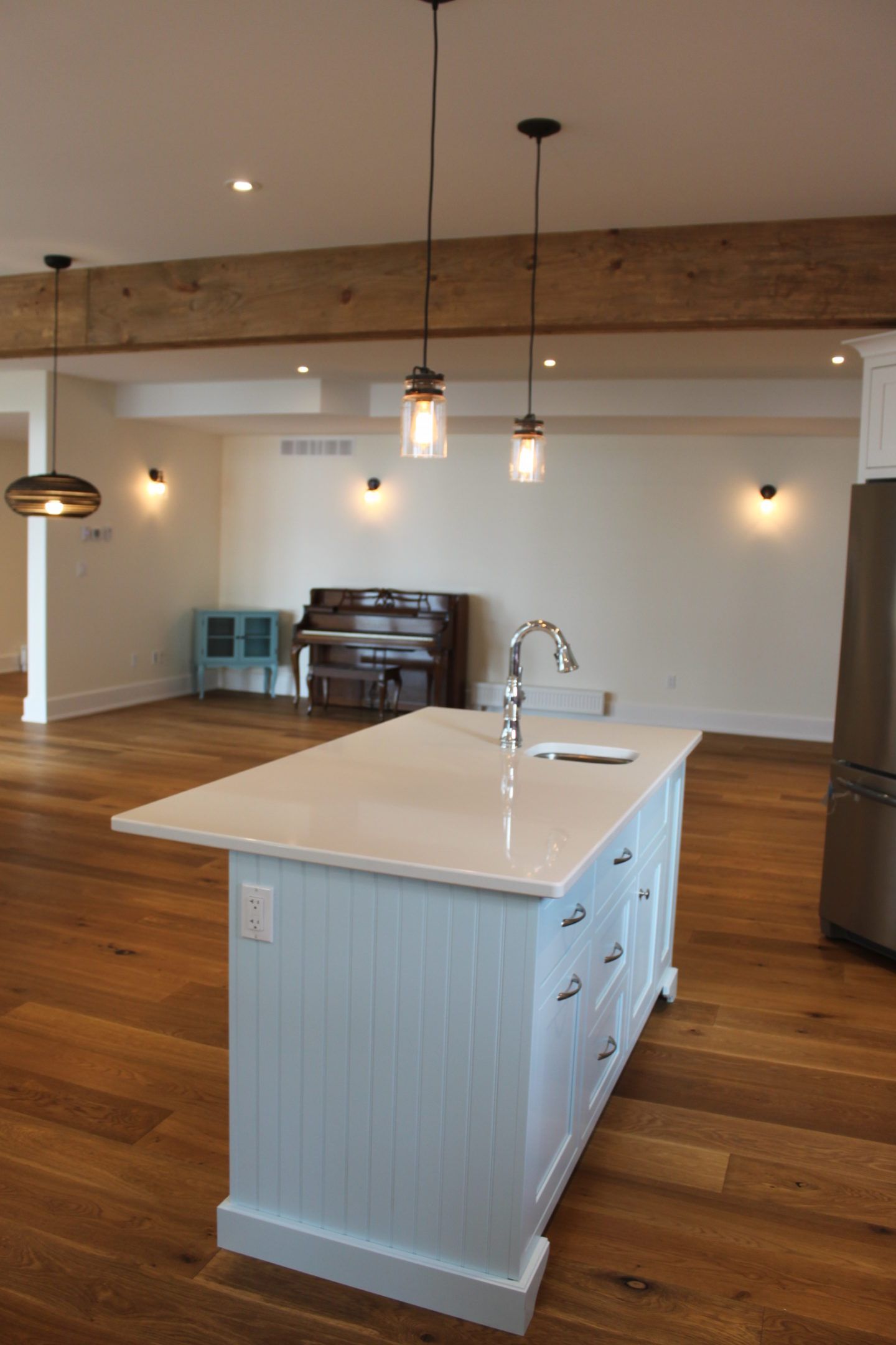 Modern kitchen with white island, pendant lights, wooden floors, and exposed beam ceiling