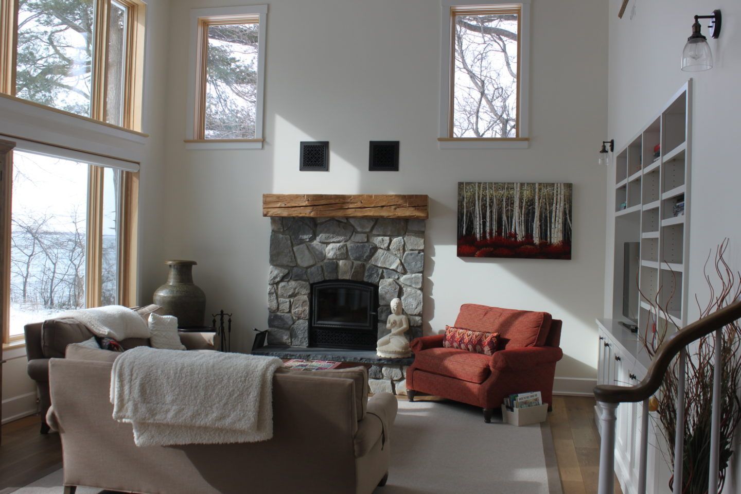 Bright living room with tall windows, stone fireplace, beige sofa, and orange chair