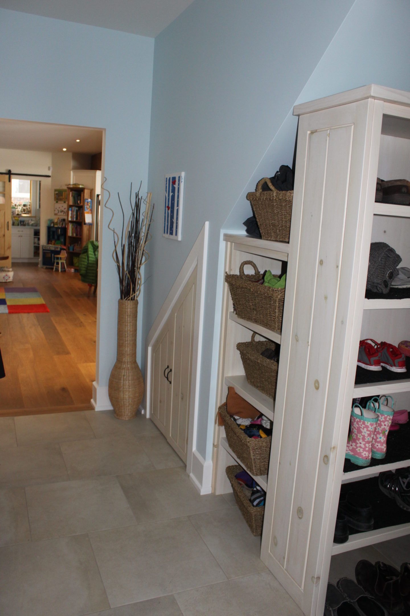 Hallway with light blue walls, staircase, and white shelving unit with baskets and folded clothes.