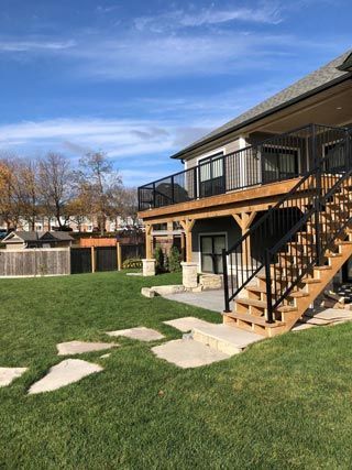Backyard with house deck, stairs, and stone stepping path over green lawn under blue sky