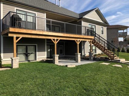 Backyard view of a raised deck with stairs, patio below, and a grassy lawn beside a house