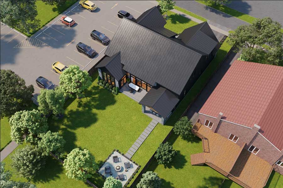 Aerial view of a house with a dark roof, green lawn, parking lot, and neighboring brick building.