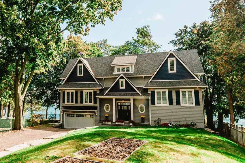 Large gray house with black trim and a front porch, surrounded by trees and a green lawn.