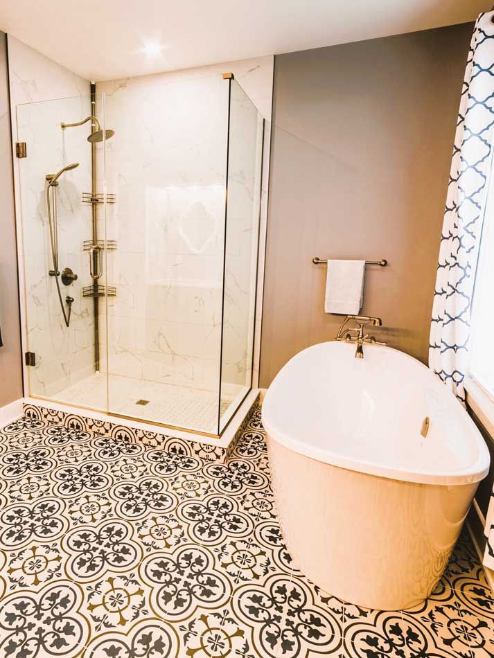 Bathroom with black-and-white patterned tile, glass shower, and freestanding tub by a window