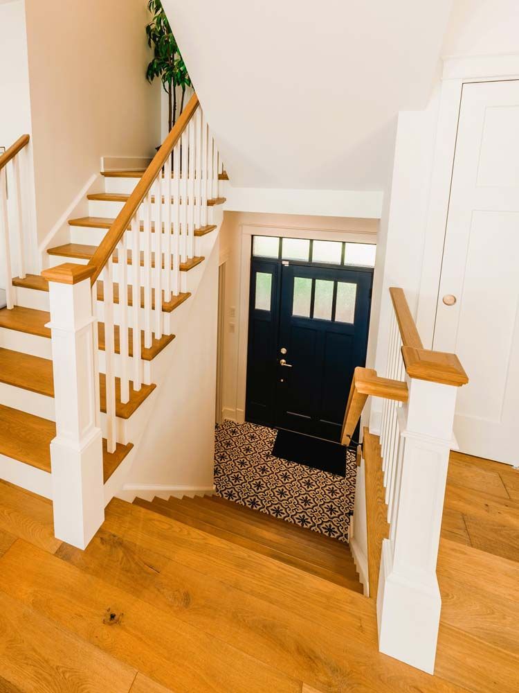 Stairwell landing with white railings, light wood steps, and a black front door below.