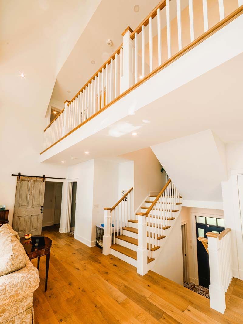 Bright living room with wooden floors, staircase, loft balcony, and white walls
