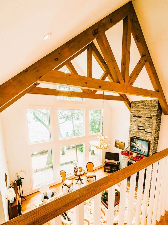 Bright loft living room with exposed wood beams, large windows, white walls, and stone fireplace
