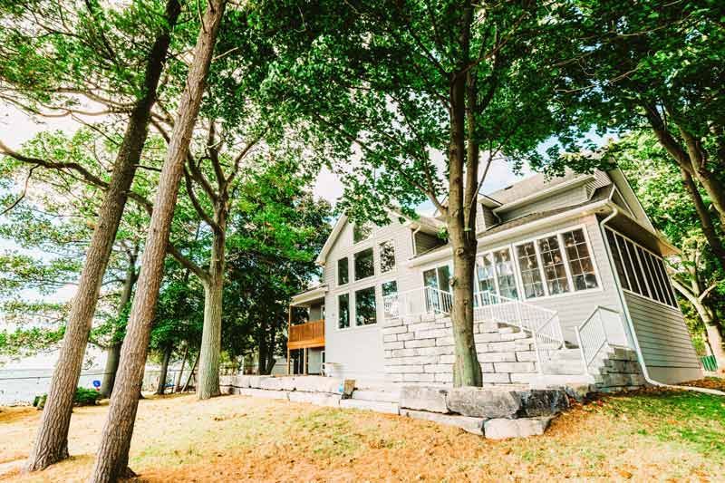 White house with screened porch among tall trees on a leafy hillside